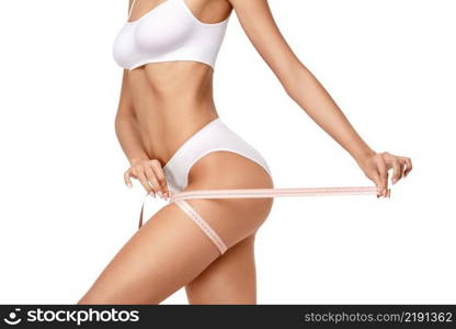 Slim long woman’s legs isolated on white background - waist measurement. Slim tanned woman’s body over gray background - waist measurement