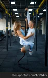 Slim love couple is hanging on a rope, training in gym. Athletic man and woman on workout in sport club, active healthy lifestyle, physical wellness. Love couple is hanging on a rope, training in gym