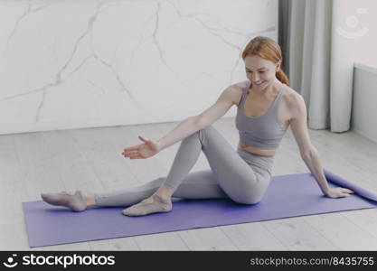 Slim sporty european girl is stretching on mat. Woman is practicing gymnastics. Concept of fitness classes at home. Sport rehabilitation. Coronavirus quarantine and healthy lifestyle.. Slim sporty girl is stretching on mat. Fitness classes at home. Sport rehabilitation and health.