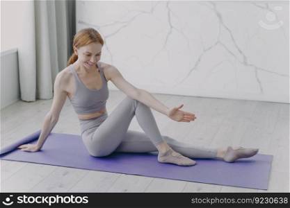 Slim sporty european girl is stretching on mat. Woman is practicing gymnastics. Concept of fitness classes at home. Sport rehabilitation. Coronavirus quarantine and healthy lifestyle.. Slim sporty girl is stretching on mat. Fitness classes at home. Sport rehabilitation and health.