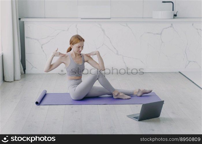 Slim sporty girl is stretching on mat. Concept of distance learning and remote fitness classes on video. Physical therapy and yoga at home. Sport teacher has online lesson.. Sport teacher has online lesson and stretching on mat. Physical therapy and yoga at home.