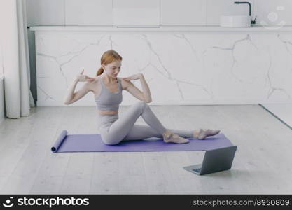 Slim sporty girl is stretching on mat. Concept of distance learning and remote fitness classes on video. Physical therapy and yoga at home. Sport teacher has online lesson.. Sport teacher has online lesson and stretching on mat. Physical therapy and yoga at home.