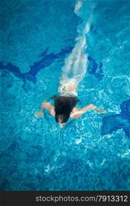 Slim woman covered in long white fabric swimming underwater at pool