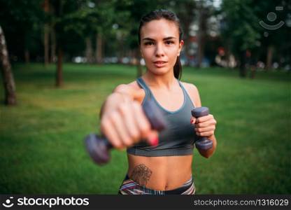 Slim woman exercise with dumbbell in summer park. Sporty girl on outdoors morning workout. Slim woman exercise with dumbbell in summer park