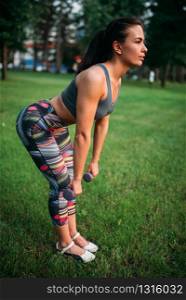 Slim woman exercise with dumbbell in summer park. Sporty girl on outdoors morning workout. Slim woman exercise with dumbbell in summer park