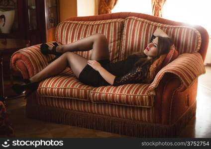 Slim woman in short dress lying on red couch
