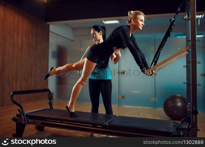 Slim woman in sportswear and instructor, pilates training with ball on exercise machine in gym. Fitness workuot in sport club. Athletic female person, aerobics indoor, body stretching. Slim woman and instructor, pilates training