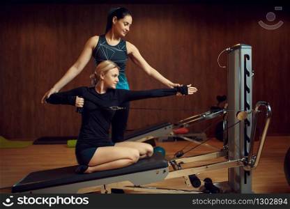 Slim woman in sportswear on pilates training with instructor on exercise machine in gym. Fitness workuot in sport club. Athletic female person, aerobics indoor, body stretching. Slim woman on pilates training with instructor