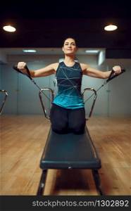 Slim woman in sportswear, pilates training on exercise machine in gym, front view. Fitness workuot in sport club. Athletic female person, aerobics indoor, body stretching. Pilates training on exercise machine in gym