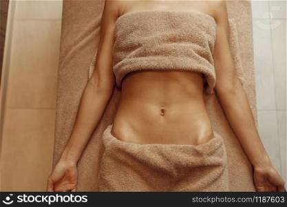 Slim woman in towel lying on massage table, top view. Massaging and relaxation, body and skin care. Female person relaxing in spa salon