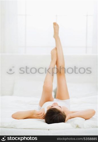 Slim woman laying on bed with rised legs. Rear view