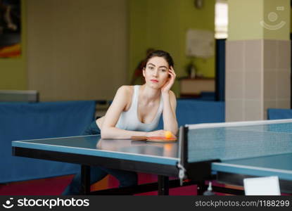 Slim woman poses at the ping pong table indoors. Female person in sportswear, training in table-tennis club