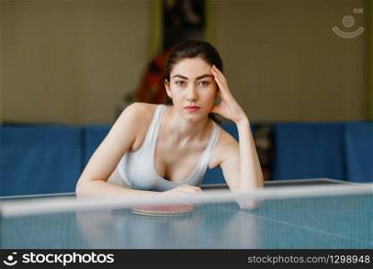 Slim woman poses at the ping pong table indoors. Female person in sportswear, training in table-tennis club. Slim woman poses at the ping pong table indoors