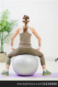 Slim woman sitting on fitness ball back to camera