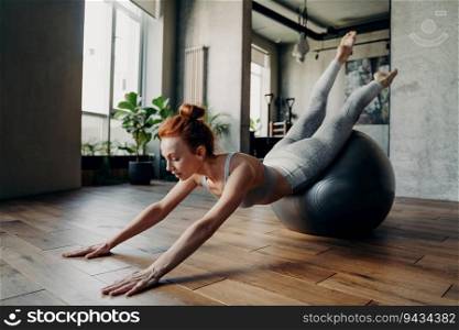 Slim woman stretches on exercise pilates ball in fitness studio or gym. Focuses on breath and muscle sensations during workout. Sportive and determined.