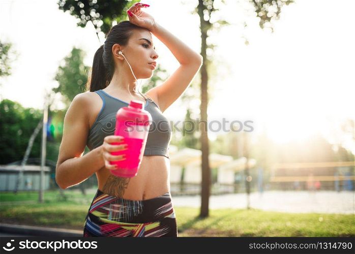 Slim woman with sport bottle, training in summer park. Girl on outdoors workout