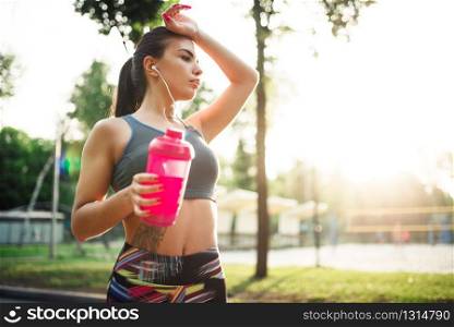 Slim woman with sport bottle, training in summer park. Girl on outdoors workout