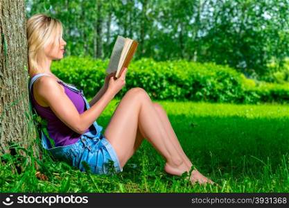 slim young girl reading a book sitting near a tree