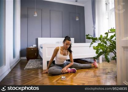 Slim young sportswoman in sportswear doing stretching exercise before workout while sitting on floor at home