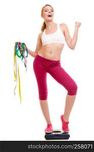 Slimming and weight loss success. Happy young woman girl measuring with tape measures on weighing scale clenching fists. Healthy lifestyle concept. Isolated on white.. Woman clenching fists measuring on weighing scale.