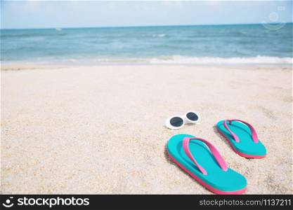 slipper of foot in sandals shoes with sunglasses and Blue ocean wave water distribution on sandy white beach,Sea background.The color of the water and beautifully. travel nature holiday summer concept