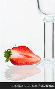 Slit strawberry and empty sparkling wine glass with reflection, white background.