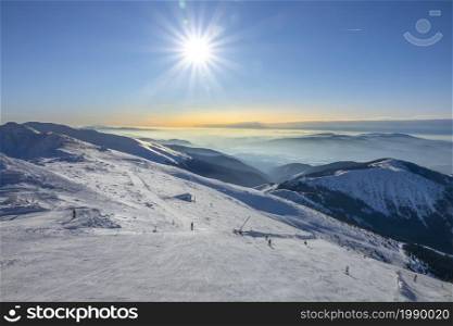 Slovakia. Winter ski resort Jasna. Bright sun in the blue sky over the ski slope. Mountain peaks and fog on the horizon. Bright Sun Over the Ski Slope and Fog Among the Mountain Peaks on the Horizon