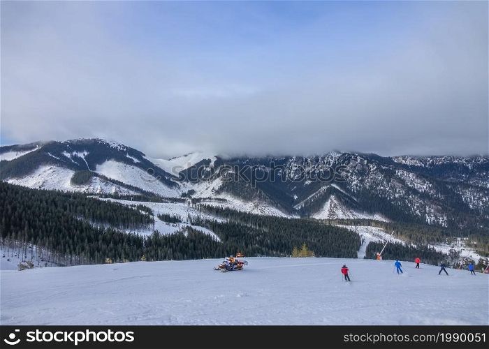 Slovakia. Winter ski resort Jasna. Skiers and a rescue snowmobile on the ski slope. Low cloud hides mountain peaks. Skiers and a Rescue Snowmobile Against the Backdrop of Mountain Peaks Hidden by a Low Cloud