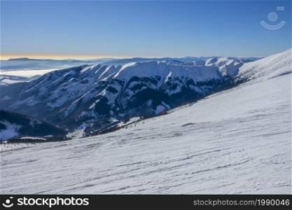 Slovakia. Winter ski resort Jasna. Sunny weather and blue sky over an empty wide ski slope. Mountain peaks and fog on the horizon. Sunny Weather Over the Ski Slope and Fog Among the Mountain Peaks on the Horizon
