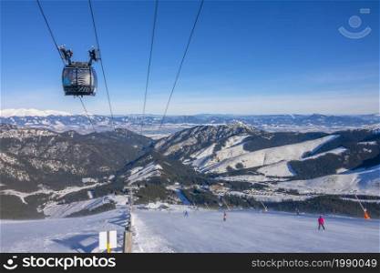 Slovakia. Winter ski resort Jasna. Sunny weather and blue sky over the ski slope. Ski lift and panorama of snow-capped mountain peaks on the horizon. Sunny Weather Over the Ski Slope and Panorama of Snow-Capped Mountains