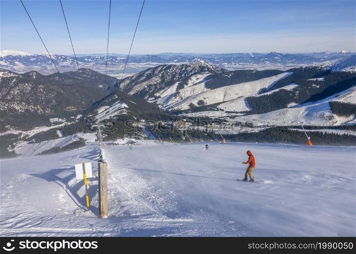 Slovakia. Winter ski resort Jasna. Sunny weather and blue sky over the ski slope. Snowboarder in snow drift and panorama of mountain peaks on the horizon. Snowboarder on a Sunny Ski Slope With Snowy Blizzard and a Panorama of Mountains