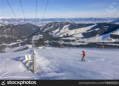 Slovakia. Winter ski resort Jasna. Sunny weather and blue sky over the ski slope. Snowboarder in snow drift and panorama of mountain peaks on the horizon. Snowboarder on a Sunny Ski Slope With Snowy Blizzard and a Panorama of Mountains