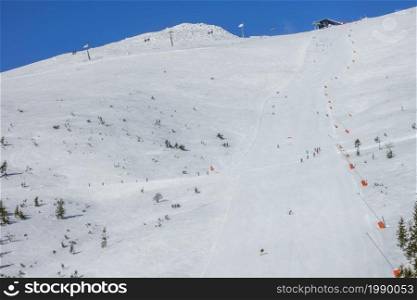 Slovakia. Winter ski resort Jasna. Sunny weather on a wide ski slope. Ski lift, several skiers and snow generators. Ski Lift, Skiers and Snow Guns on a Wide Ski Slope