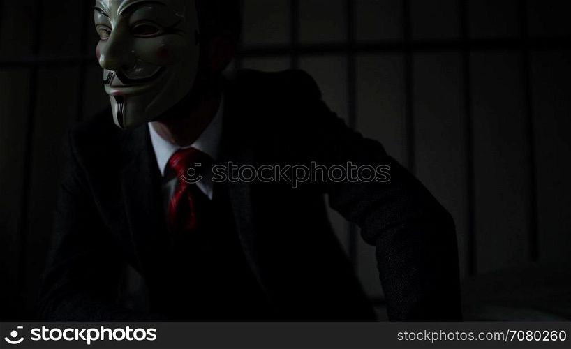 Slow dolly shot of Anonymous hacker man in prison