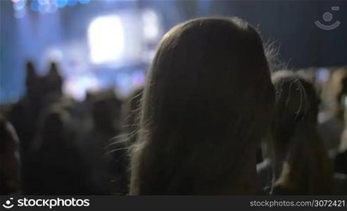 Slow motion and close-up shot of a blonde woman putting on wireless headphones in crowded nightclub. View from the back