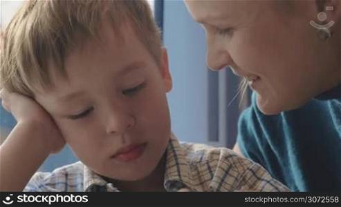 Slow motion and close-up shot of a child and mother traveling by train. Boy is excited with playing a game, mother kissing him gently