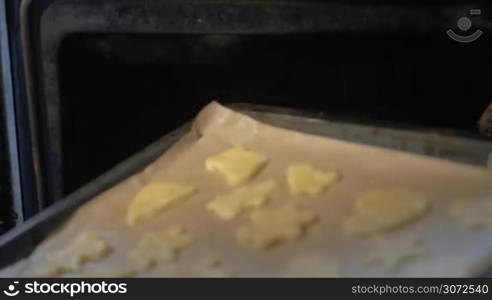 Slow motion and close-up shot of a hand in oven mitt putting baking tray with cookie dough into the hot oven and closing the door. Home-baked treats