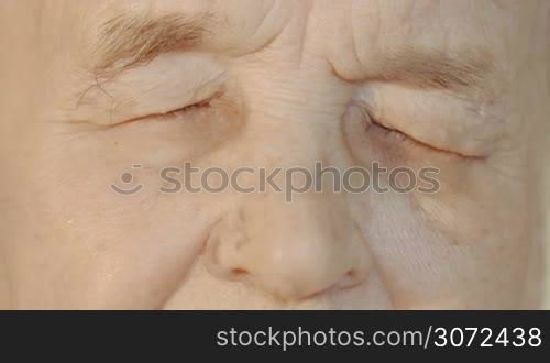 Slow motion and close-up shot of elderly womans face. She opening eyes looking to the camera and closing them again