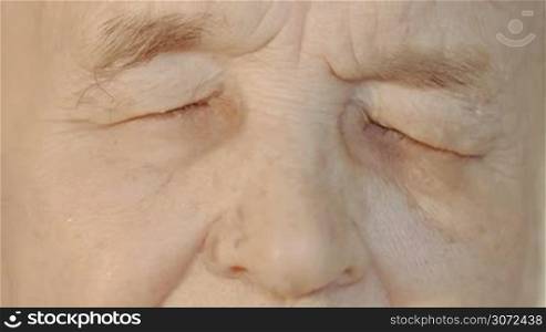Slow motion and close-up shot of elderly womans face. She opening eyes looking to the camera and closing them again