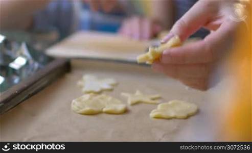 Slow motion and close-up shot of female hand putting star cookie dough on the baking tray with other cutouts. Home-baked treats