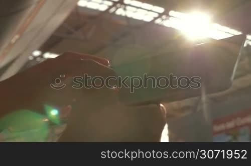 Slow motion and close-up shot of female hands using tablet PC at the station. Bright sun flare and metal roof structure in background