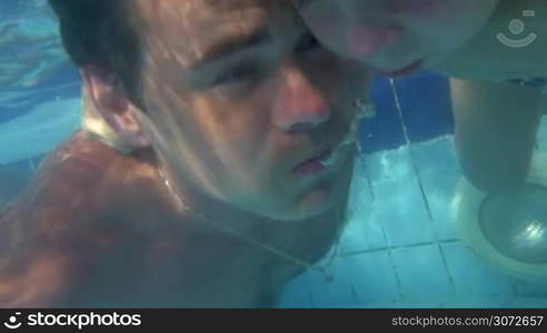 Slow motion and close-up shot of young father and little son diving together in the swimming pool and coming out from the water