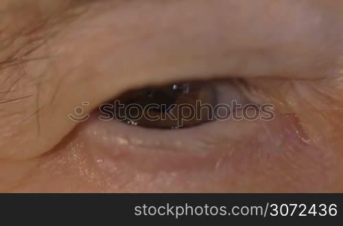 Slow motion and extreme close-up shot of a blinking brown eye of an aged woman with wrinkled skin