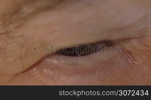 Slow motion and extreme close-up shot of a senior womans eye looking to the camera. Tired look and wrinkled skin