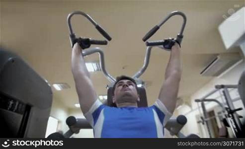 Slow motion and low angle shot of a young sportsman exercising on shoulder press machine. Being strong and healhy is easy with regular sports
