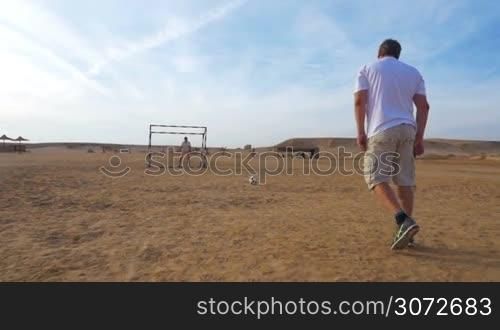 Slow motion and steadicam shot of a man kicking a goal during the playing football on resort area. Outdoor sports and activities