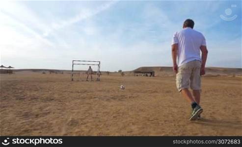 Slow motion and steadicam shot of a man kicking a goal during the playing football on resort area. Outdoor sports and activities