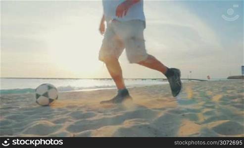 Slow motion and steadicam shot of a man playing football on the beach. He dribbling on the sand against sea and sunset background