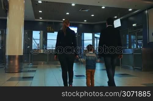 Slow motion back shot of mother, father and son holding hands and walking in empty airport terminal