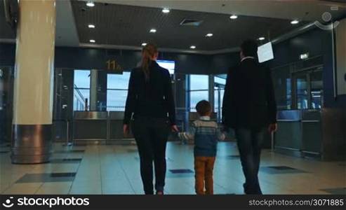 Slow motion back shot of mother, father and son holding hands and walking in empty airport terminal